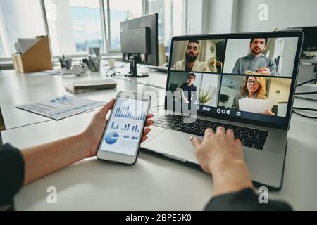 Meeting via video conferencing app: manager using sales analysis graph while discussing strategy with colleagues via video chat on laptop Stock Photo