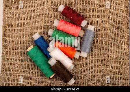 Several coils of multicolored sewing thread against a background of coarse-textured burlap. Close up Stock Photo