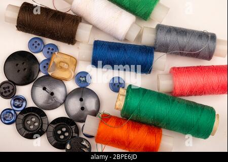 Several reels of multicolored sewing thread and multicolored buttons of different sizes on a white background. Close up Stock Photo