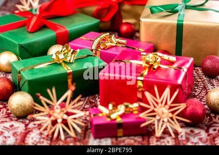 Christmas gifts wrapped in red, green and gold with plain-colored bows amidst baubles and straw stars. Tightly-cropped shot with focus on magenta gift Stock Photo