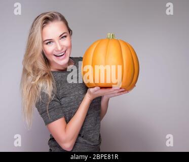 Portrait of happy cheerful woman holding in hand big orange pumpkin isolated on gray background, Thanksgiving day celebration Stock Photo