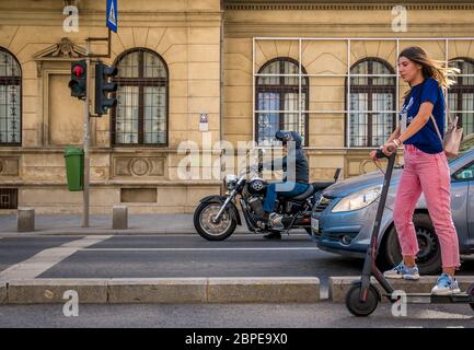 Bucharest/Romania - 05.16.2020: A biker on a motorcycle and a girl rigind an electric scooter at the stoplight. . People enjoying a nice day in the ce Stock Photo