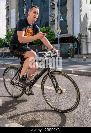 Bucharest/Romania - 05.16.2020: Man texting on his smartphone while riding a bicycle in the center of Bucharest. People enjoying a nice day in the cen Stock Photo