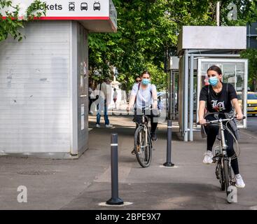 Bucharest/Romania - 05.16.2020: Two girlsl wearing face masks riding bicycles, People enjoying a nice dayin the center of Bucharest after the coronavr Stock Photo