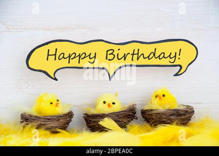 Three Sitting Easter Chicks In Easter Baskets Or Nest With Yellow Feathers On White Wooden Background With Comic Speech Balloon With English Text Happ Stock Photo