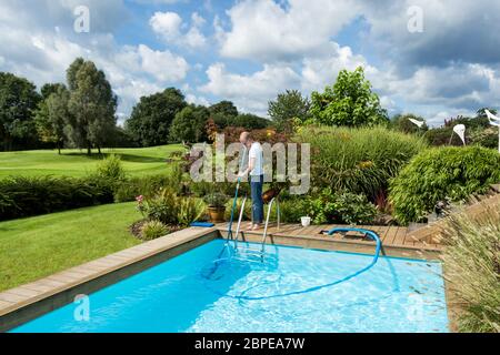 Junger mann reinigt ein schwimmbad swimmingpool mit einer Teleskopbürste im Sommer im Freien Stock Photo