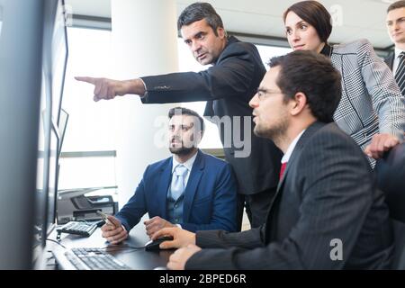 Business team looking at data on multiple computer screens in corporate office. Businessman pointing on screen. Business people trading online. Busine Stock Photo