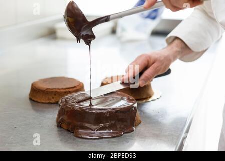 pastry chef covering cake with melted chocolate Stock Photo