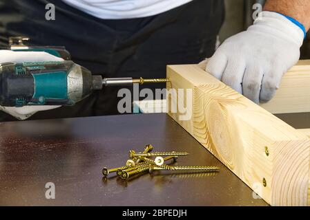 Carpenter, a man works with a cordless screwdriver. Drills and tightens the screws with a cordless drill. Working with wood in the carpentry workshop. Stock Photo