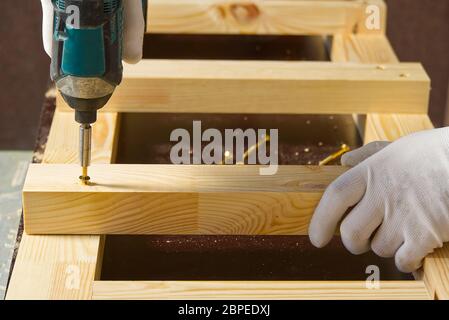 Carpenter, a man works with a cordless screwdriver. Drills and tightens the screws with a cordless drill. Working with wood in the carpentry workshop. Stock Photo