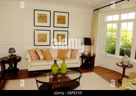 A nice living room with a large window, sofa and chairs with pictures on the wall and an glass table in a new house. Stock Photo