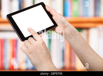 finger touches tablet pc with cut out screen on front of book shelves Stock Photo