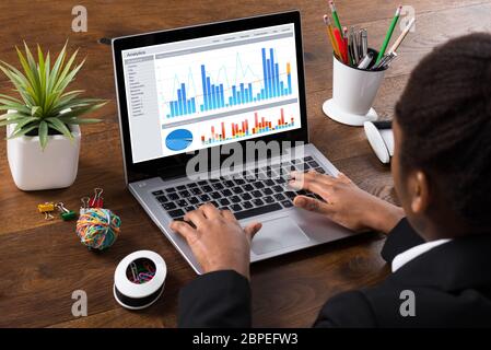 Young African Businesswoman Analyzing Graph On Laptop In Office Stock Photo