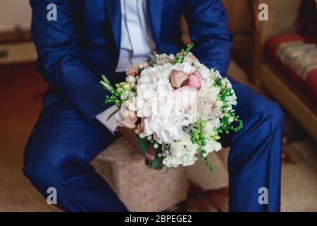 fiance in a dark blue suit holds a wedding bouquet made of peonies Stock Photo