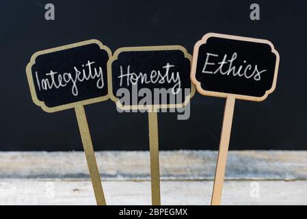 Business message Integrity, Honesty, Ethics written with chalk on wooden mini blackboard labels, defocused chalkboard and wood table in background Stock Photo