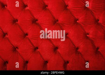 Red velvet capitone textile background, retro Chesterfield style checkered soft tufted fabric furniture diamond pattern decoration with buttons, close Stock Photo