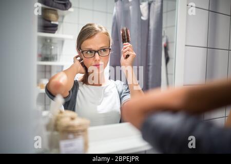 Young woman brushing healthy hair in front of a mirror morning before leaving for work (color toned image; shallow DOF) Stock Photo