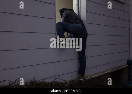 Rear View Of A Burglar Entering In A House Through A Window Stock Photo