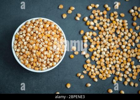Raw corn kernel in bowl and spread around on stone, concrete background. Flat lay composition. Healthy, organic and delicious food. Stock Photo