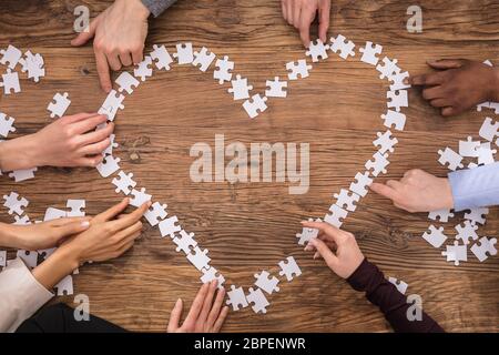 High Angle View Of Businesspeople Forming Heart Shape Sign With Jigsaw Puzzle Stock Photo