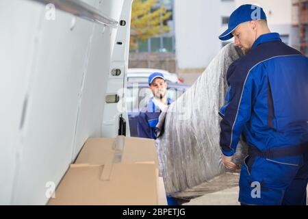Two Happy Male Movers In Uniform Unloading Furniture From Truck Stock Photo