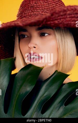 Cole up portrait of beautiful woman holding a leaf of a palm tree on a yellow background in studio Stock Photo