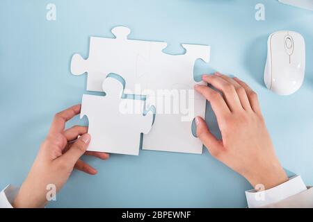 Elevated View Of A Businesswoman Joining The Jigsaw Puzzle Pieces On Blue Desk Stock Photo