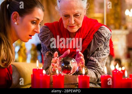 Female Fortuneteller or esoteric Oracle, sees in the future by looking into their crystal ball answering questions from client Stock Photo