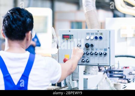 Worker pressing buttons on CNC machine control board in Asian factory Stock Photo