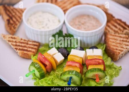Tasty snacks: roasted toast with cheese vegetables and olive on the stick. Served with two kind of sauce Stock Photo