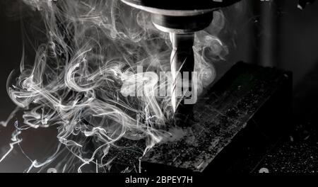 Bridgeport CNC end mill finishing a stack of steel plate with metal filings chips and heavy smoke trailing Stock Photo