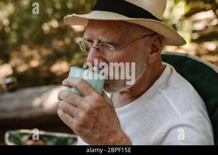Close-up of a senior man having refreshing coffee at campsite. Male traveller drinking a cup of coffee at camping trip. Stock Photo