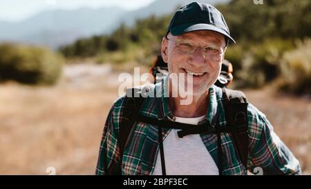 Portrait of a senior man carrying a backpack looking at camera and smiling. Fit old man on a hiking trip. Stock Photo
