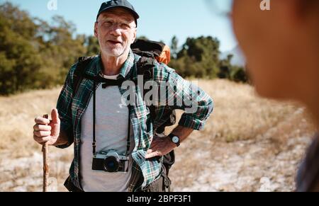 Senior man on a hiking trip talking with some one standing in front. Elderly make hiker asking for the route to a person. Stock Photo