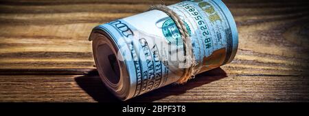 A roll of dollars on a wooden textured table in the dark illuminated by a ray of light Stock Photo