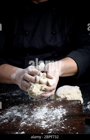 baker kneads white wheat flour dough on a brown  wooden table Stock Photo