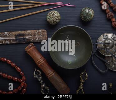 Copper singing bowl, prayer beads, stone balls and other Tibetan religious objects for meditation and alternative medicine on a black wooden backgroun Stock Photo