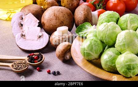 Several heads of fresh wet brussels sprouts on a wooden plate, cherry tomatoes, oil and peppers in a small spoons on a linen fabric . Stock Photo