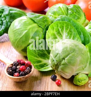 Several heads of fresh wet brussels sprouts, cherry tomatoes, peppers in a small spoon on a wooden table. Stock Photo