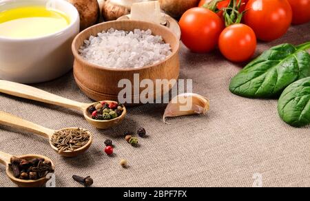 Various spices in small wooden spoons, salt, vegetable oil, cherry tomatoes, mushrooms, spinach and garlic on a linen fabric. Stock Photo