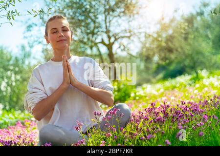 Beautiful woman doing yoga exercise outdoors, nice female in lotus pose meditating with closed eyes in beautiful blooming spring garden, healthy life Stock Photo