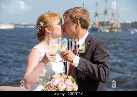 The bride and groom with glasses of champagne against the background of the river. Stock Photo