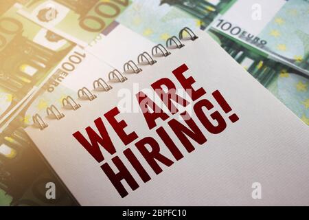 We are Hiring phrase written on page of copybook put on 100 Euro banknotes. Selective focus. HR planning business management concept Stock Photo