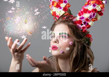 A fabulous girl in flowers holds a luminous ball. Spring or summer beauty. Beautiful woman blowing on flowers. Stock Photo