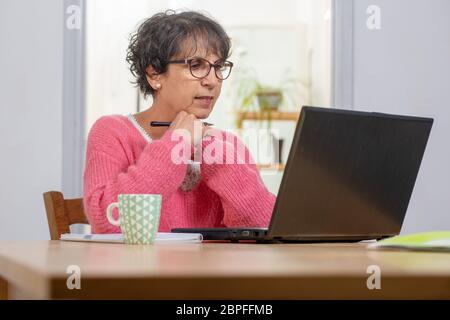 beautiful brunette mature woman dressed in pink with a laptop at home Stock Photo