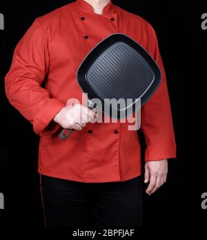 cook in red uniform holding an empty square black frying pan, black background Stock Photo