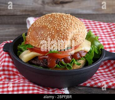 burger with a meatball and vegetables in a black round cast-iron frying pan, close up Stock Photo