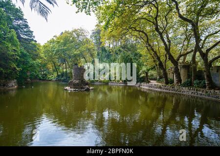 Old Duck House in the middle of a pond in a lush and verdant natural parkland at the Pena Park in Sintra, Portugal. Stock Photo