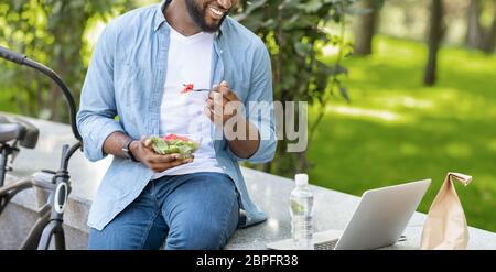 Afro Man Eating Lunch And Watching Movie On Laptop In Park Stock Photo