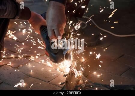 Front view of a man's hands working on a metal part of a garden bench, using an electric grinder while sparks are flying around in the industrial work Stock Photo